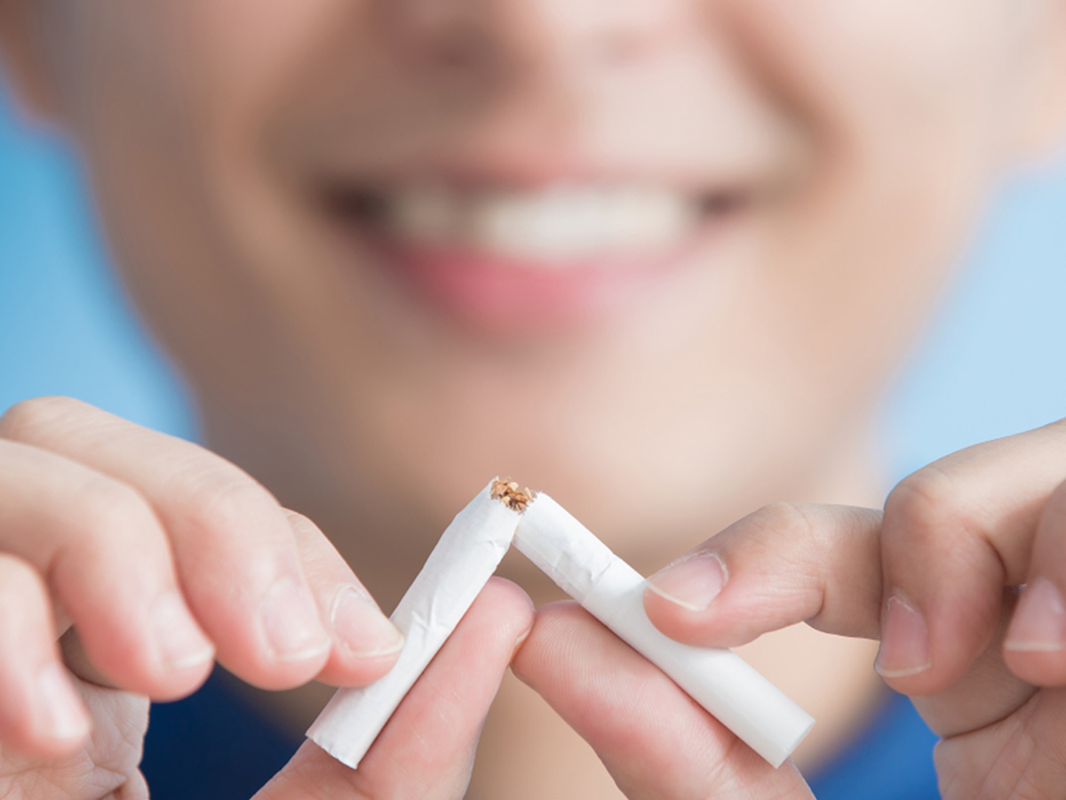 Woman smiles in blurred background while she snaps a cigarette in half close up.