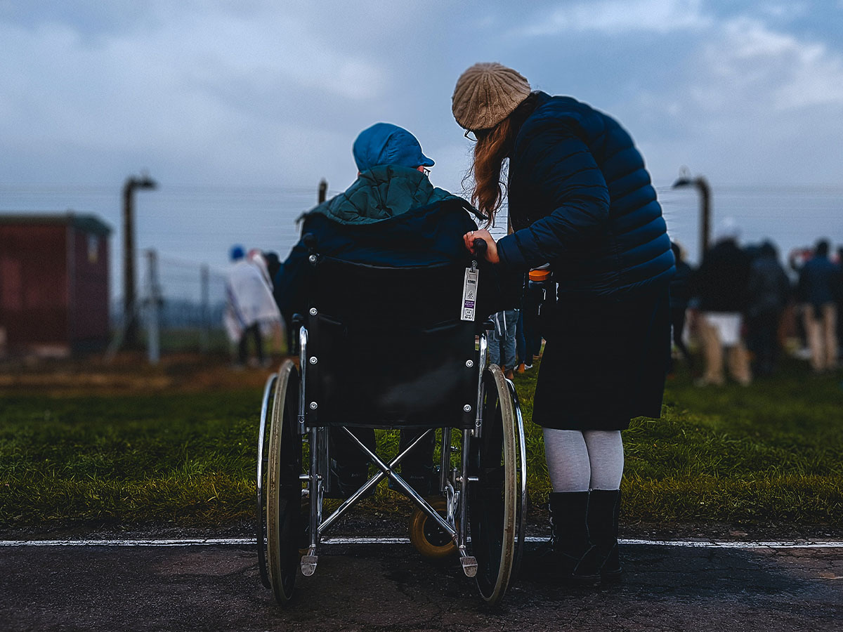 Elderly person in a wheelchair talking to a younger person standing next to them