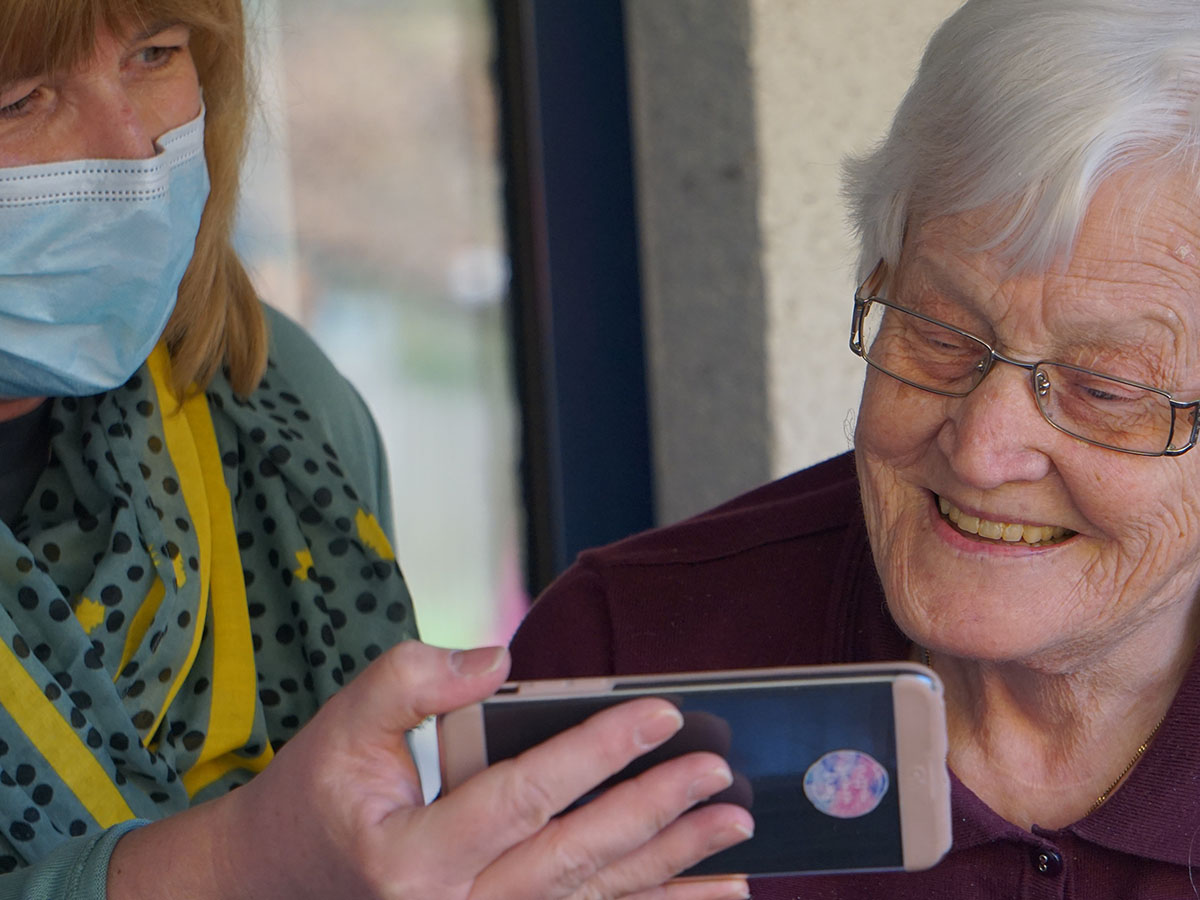 Caregiver holding a phone for an elderly woman as she watches something on it