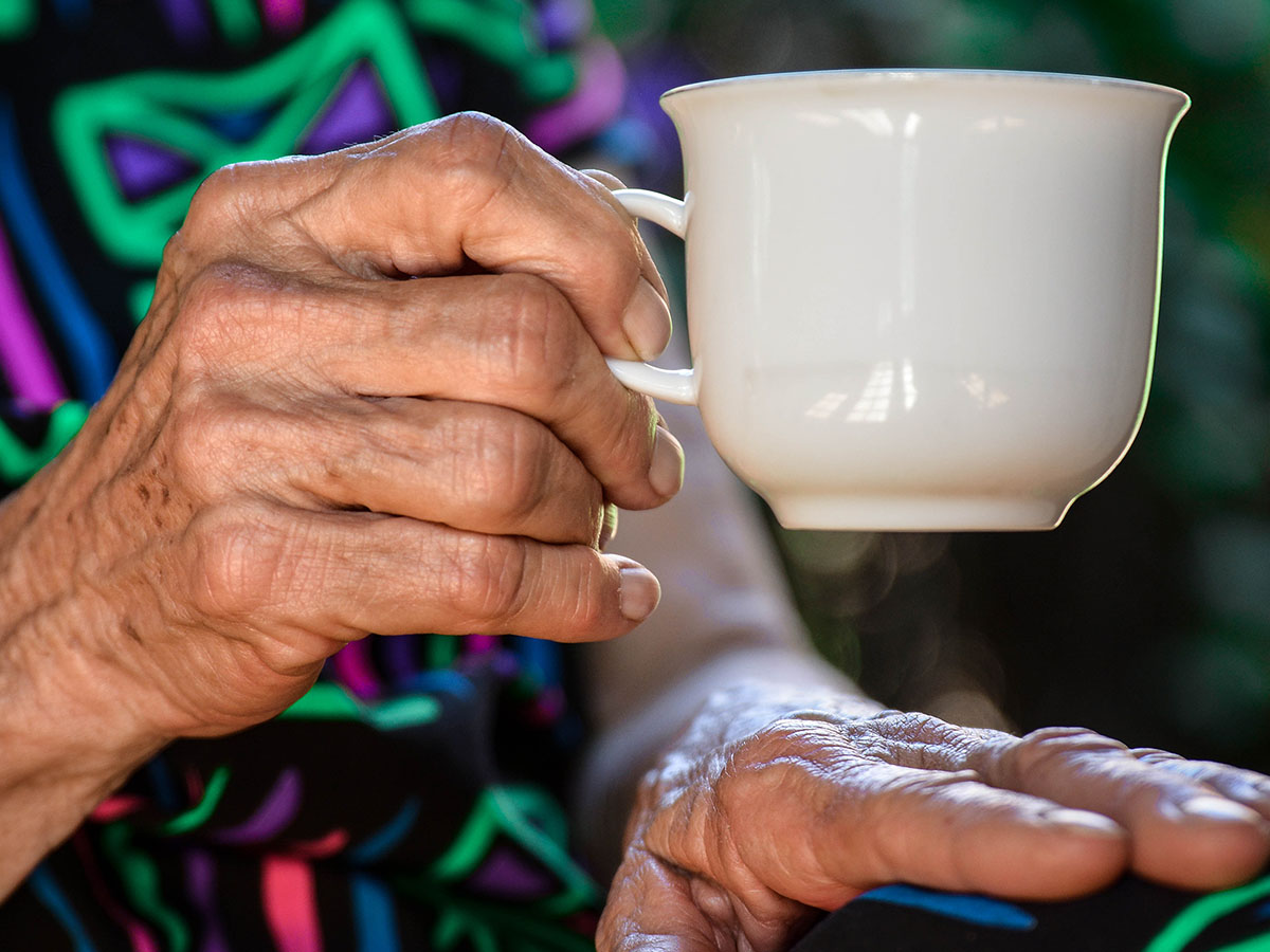 Close up of an elderly person holding a teacup in one hand