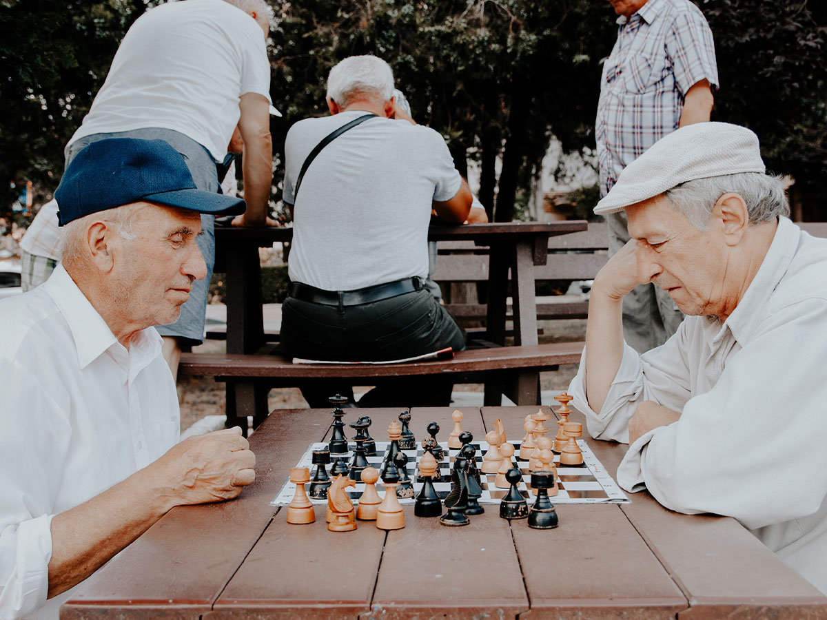 Elderly men gathered in a park playing chess on a table