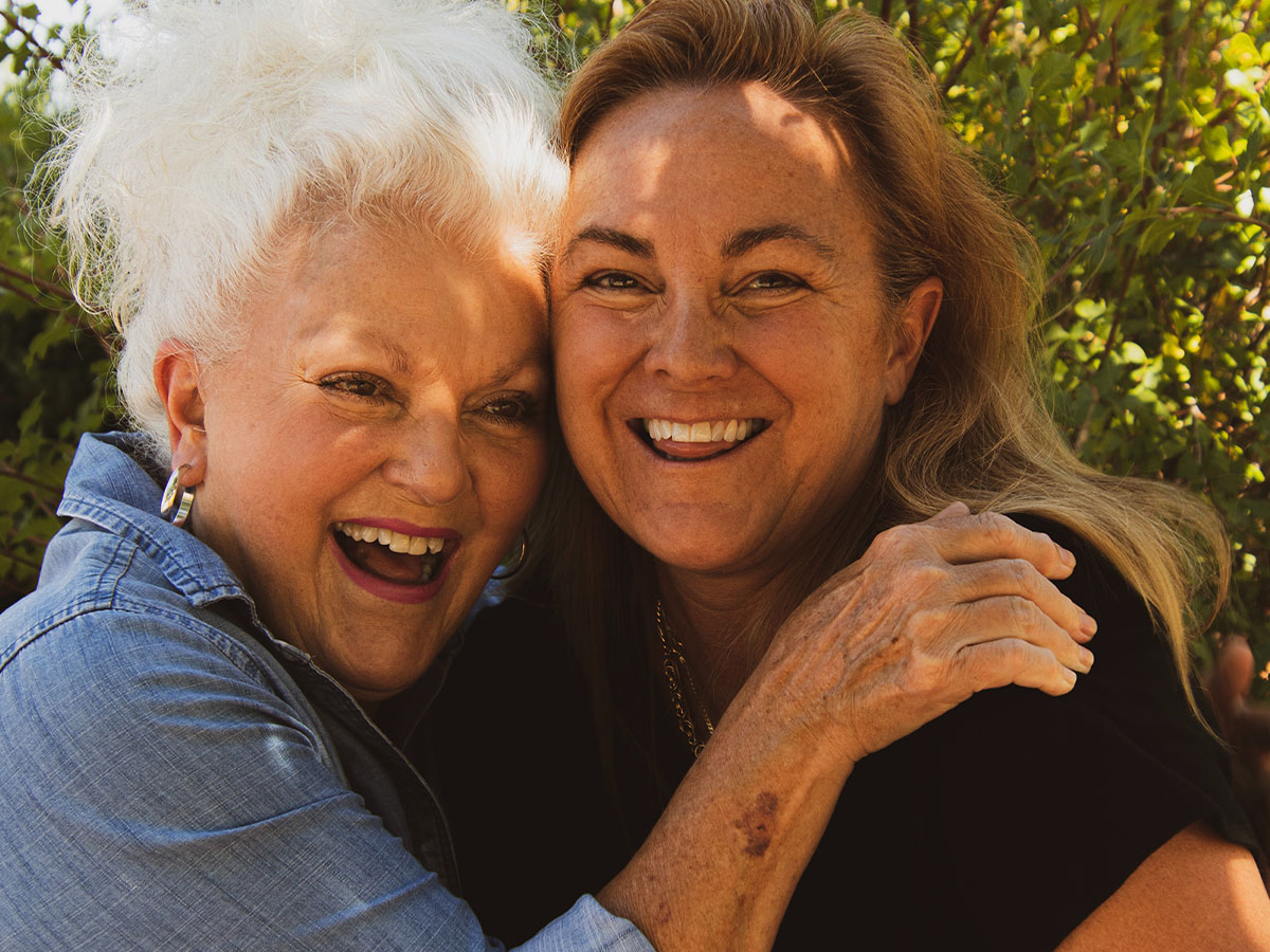 An elderly woman laughing as she hugs a younger woman